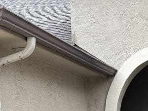 closeup of taupe gutter installed on tan stucco exterior home